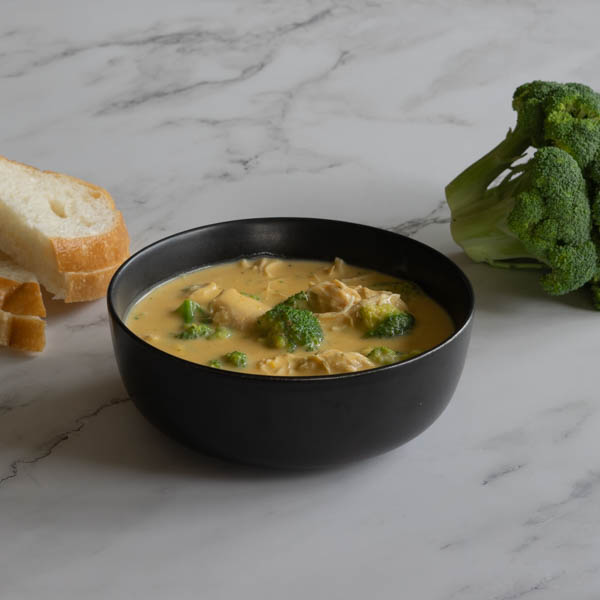 Broccoli Cheese Soup in a black bowl with bread and broccoli