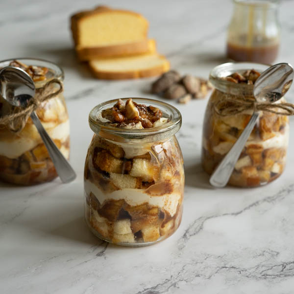 Three parfaits with a spoons, pound cake, caramel and pecans.