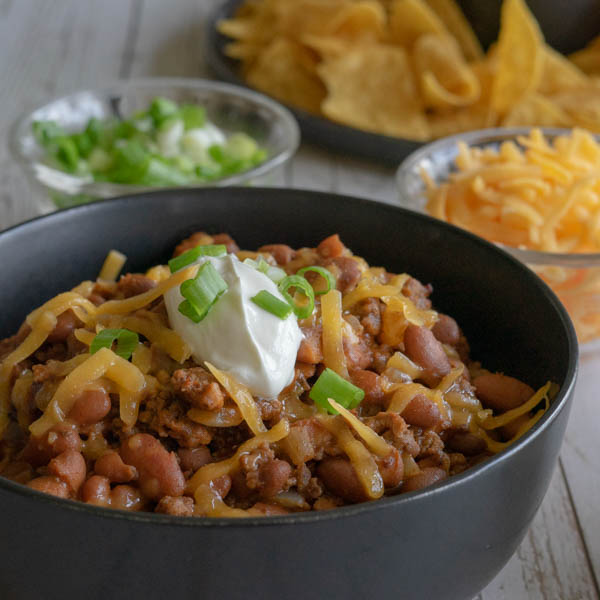 Chili with sour cream, cheese and green onions in a black bowl