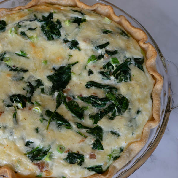 Spinach and Bacon Quiche in a glass pie dish.