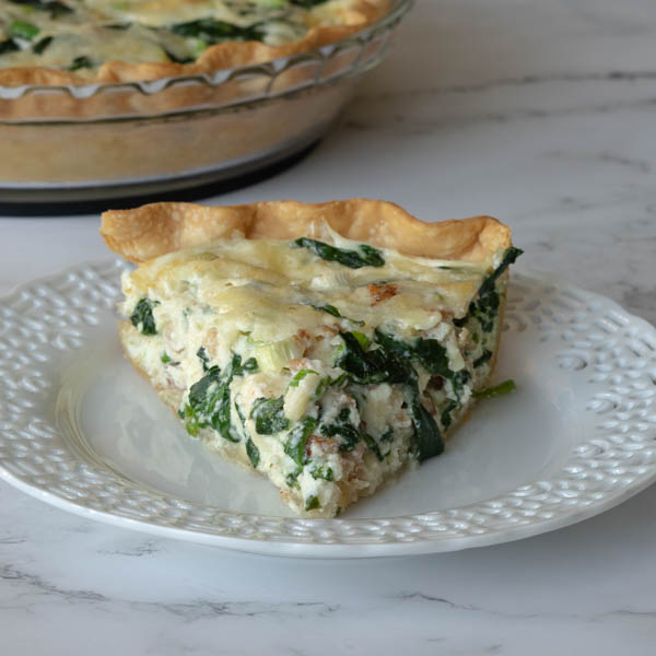 Spinach and Bacon Quiche in a glass pie dish.